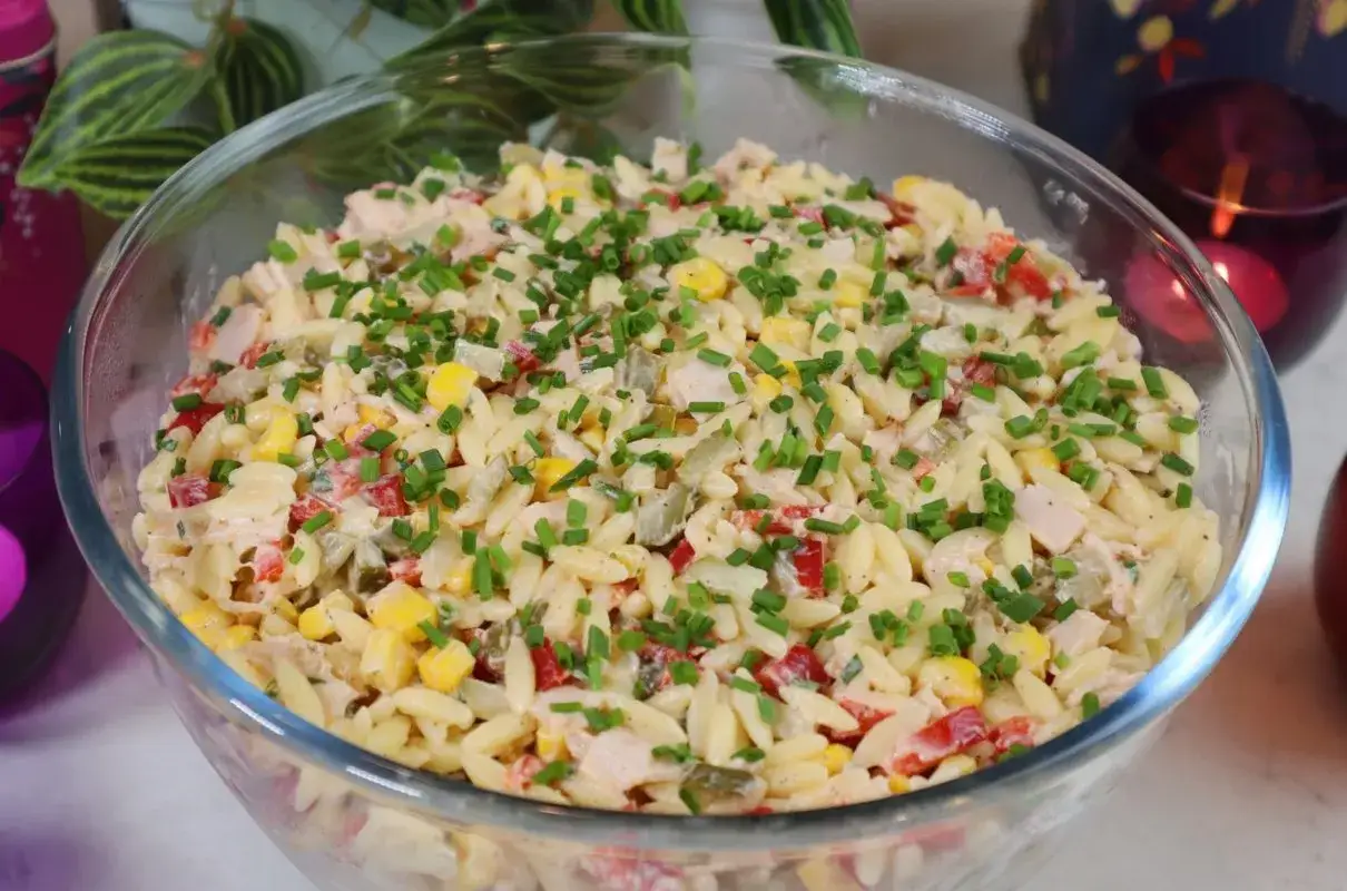 Pyszna sałatka z makaronem orzo i szynką, z kukurydzą, papryką i szczypiorkiem, podana w szklanej misie.