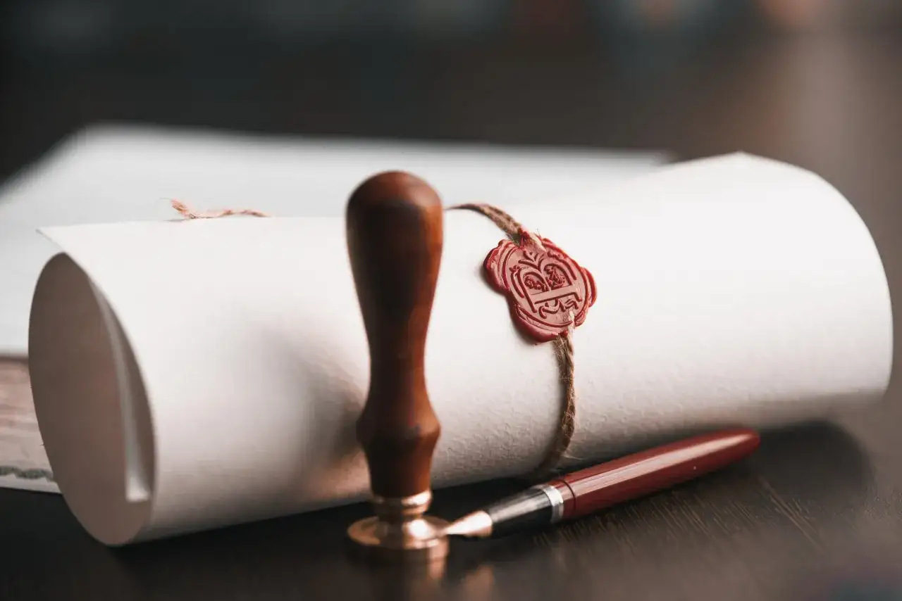 Pieczęć lakowa i pióro na zrolowanym dokumencie, symbolizujące formalne zatwierdzenie, jak absolutorium dla zarządu.