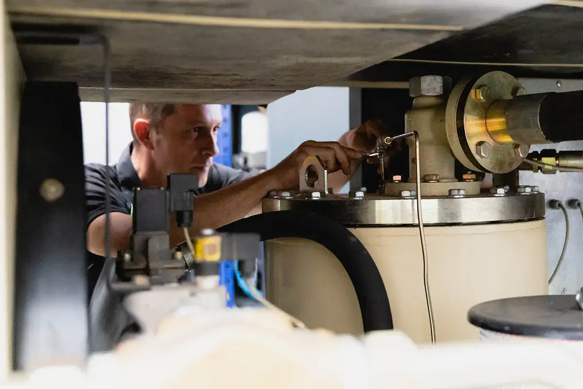 Técnico ajustando un compresor de aire. Determinar qué tiempo debe descansar el compresor del aire es crucial para su mantenimiento.