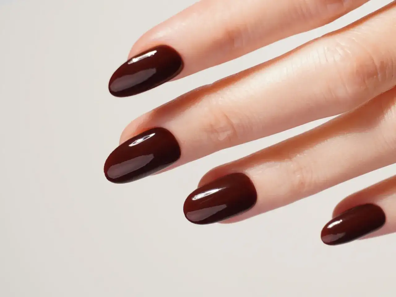 Main d'une femme aux ongles vernis d'un brun profond, couleur tendance ongle automne.