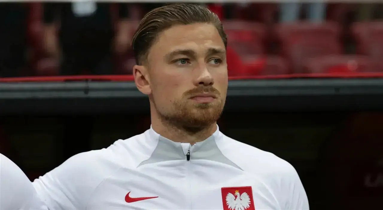 Mati Cash, polski piłkarz w białej koszulce z godłem Polski, gotowy do gry.