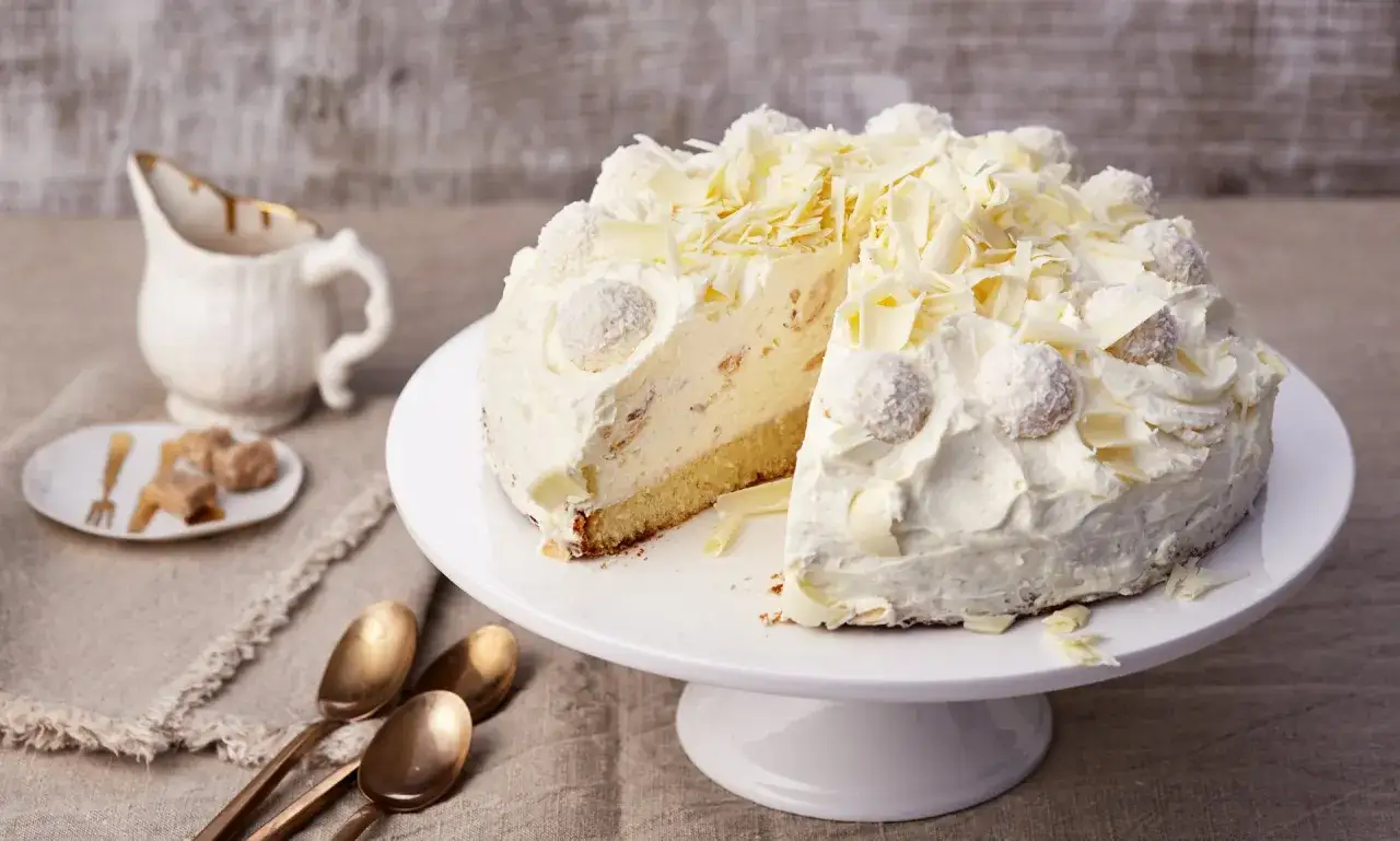 Eine köstliche Raffaello Torte, verziert mit Kokosraspeln und weißen Schokostückchen, wartet darauf, angeschnitten zu werden.