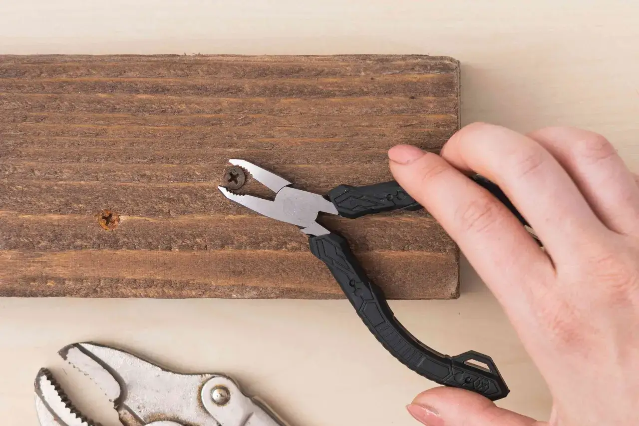 Mano usa pinzas para intentar como aflojar tuercas y tornillos agarrotados oxidados o pegados en madera.