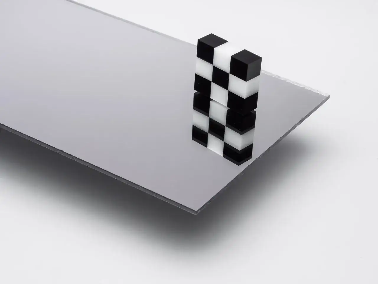 A checkerboard stack of black and white acrylic cubes sits on a reflective acrylic mirror sheet, hinting at how to cut acrylic mirror for creative projects.