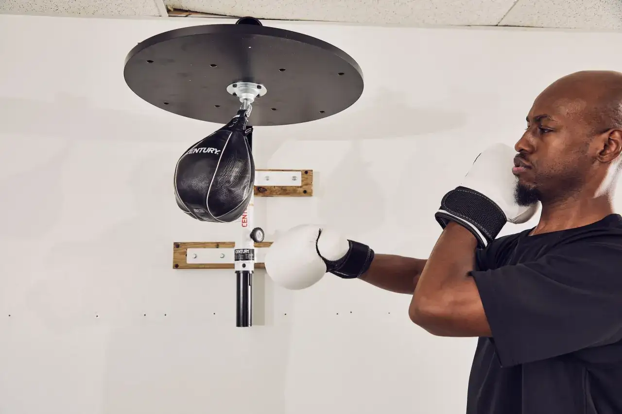 A man in white sparring gloves practices with a speed bag, a key tool for developing hand speed and coordination, distinct from heavier bag gloves.