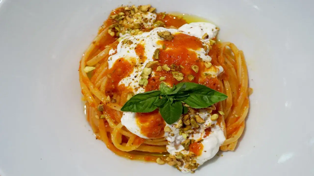 Spaghetti al pomodoro con abbondante stracciatella, pistacchi tritati e basilico fresco. Un piatto cremoso e gustoso.