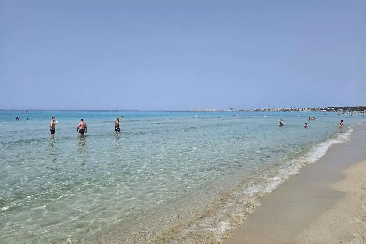 Persone godono del limpido **mare** di **Gallipoli**, con la costa in lontananza sotto un cielo azzurro.