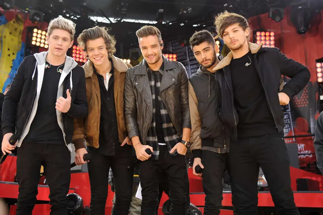Pięciu członków One Direction pozuje na scenie, gotowi do występu.