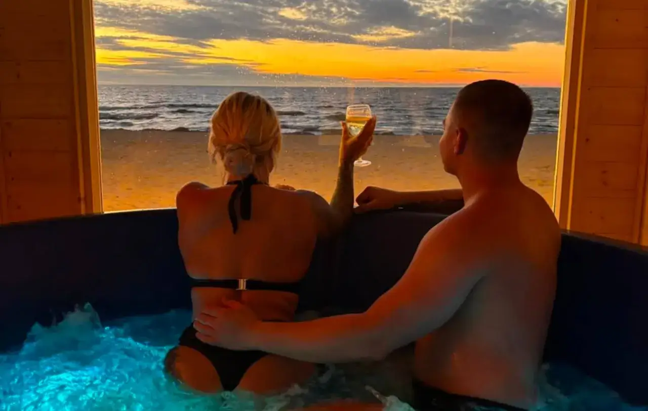 Para spędza romantyczny weekend z przyjaciółką w jacuzzi, podziwiając zachód słońca nad morzem.