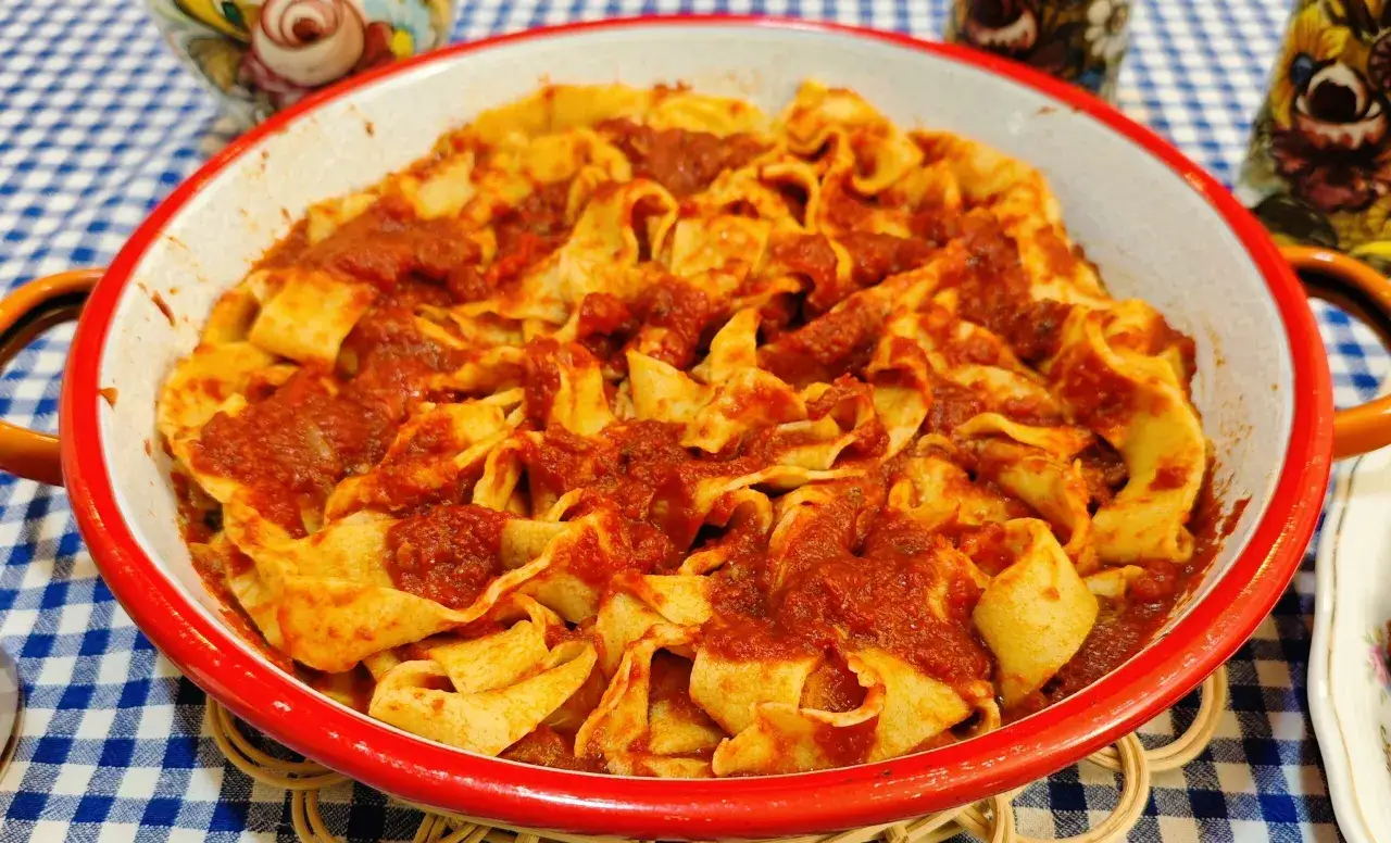 Pappardelle al ragù di papera, un piatto ricco e saporito, servito in una ciotola rossa su una tovaglia a quadri blu.