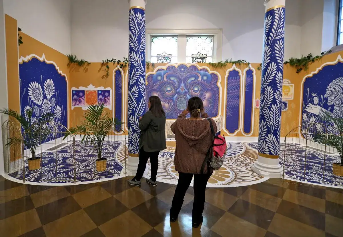 Two visitors admire a vibrant exhibition featuring intricate patterns and artwork, showcasing the talent of latin american artists.