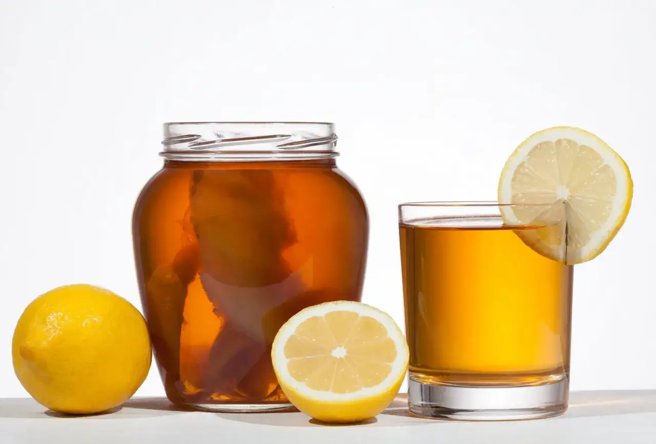 Bocal de kombucha, citrons et verre de boisson ambrée. L'origine de cette boisson fermentée est mise en avant.