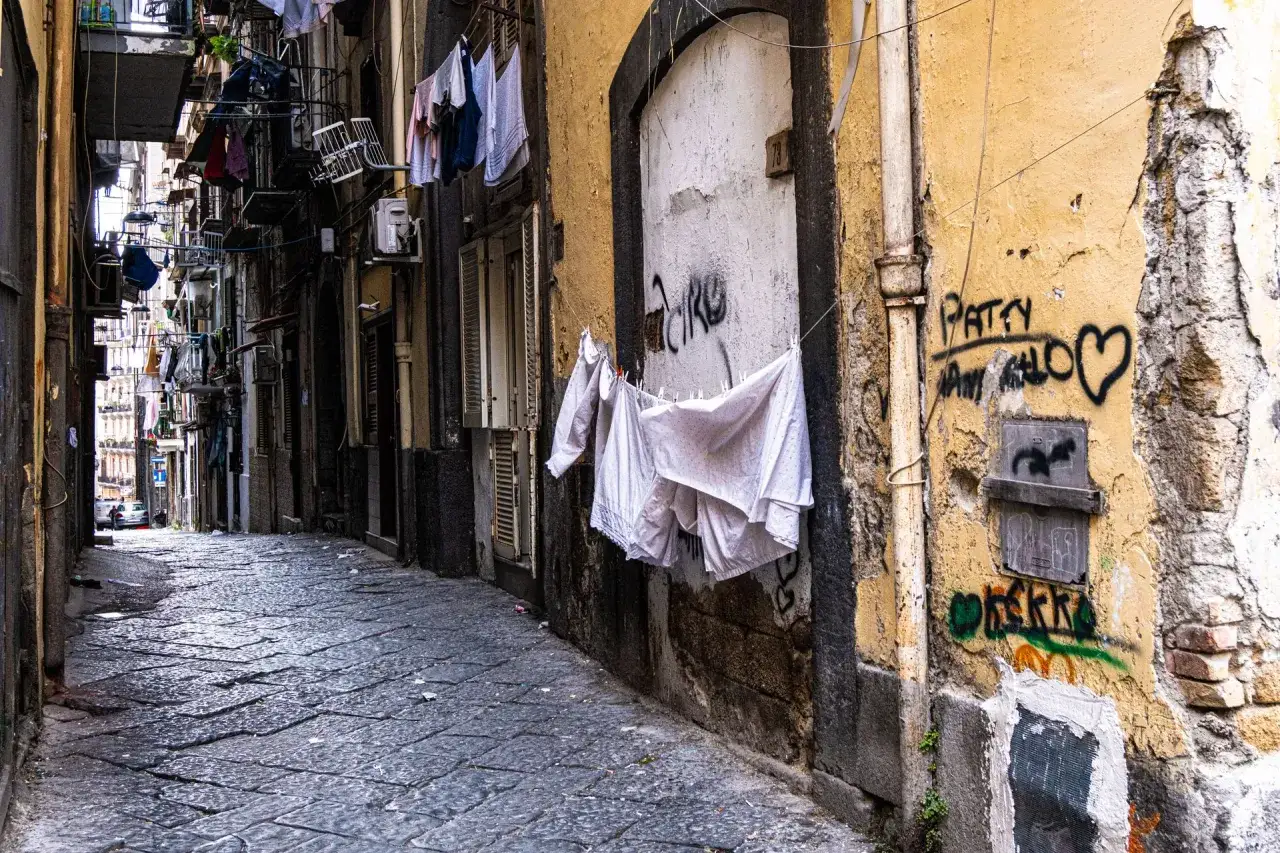 Une ruelle typique pour visiter Naples, avec du linge suspendu et des graffitis sur les murs jaunis.