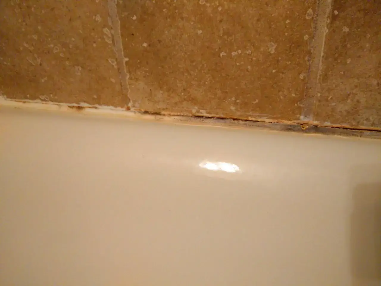 Old caulk in a shower is cracked and stained, showing the need to learn how to caulk a shower for a fresh, waterproof seal.