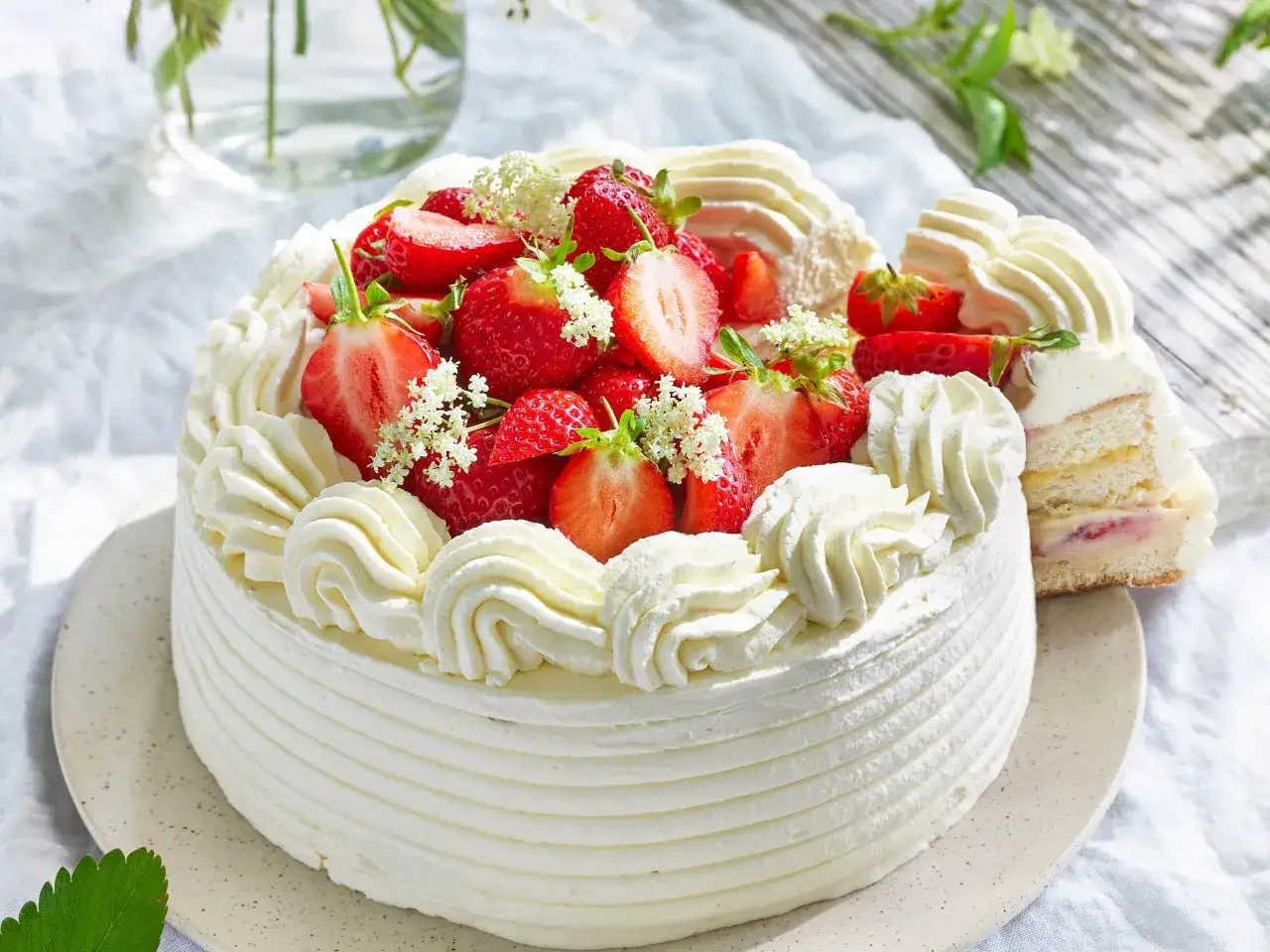 En krämig tårta dekorerad med färska jordgubbar och små vita blommor. En perfekt somrig dessert för varma dagar.