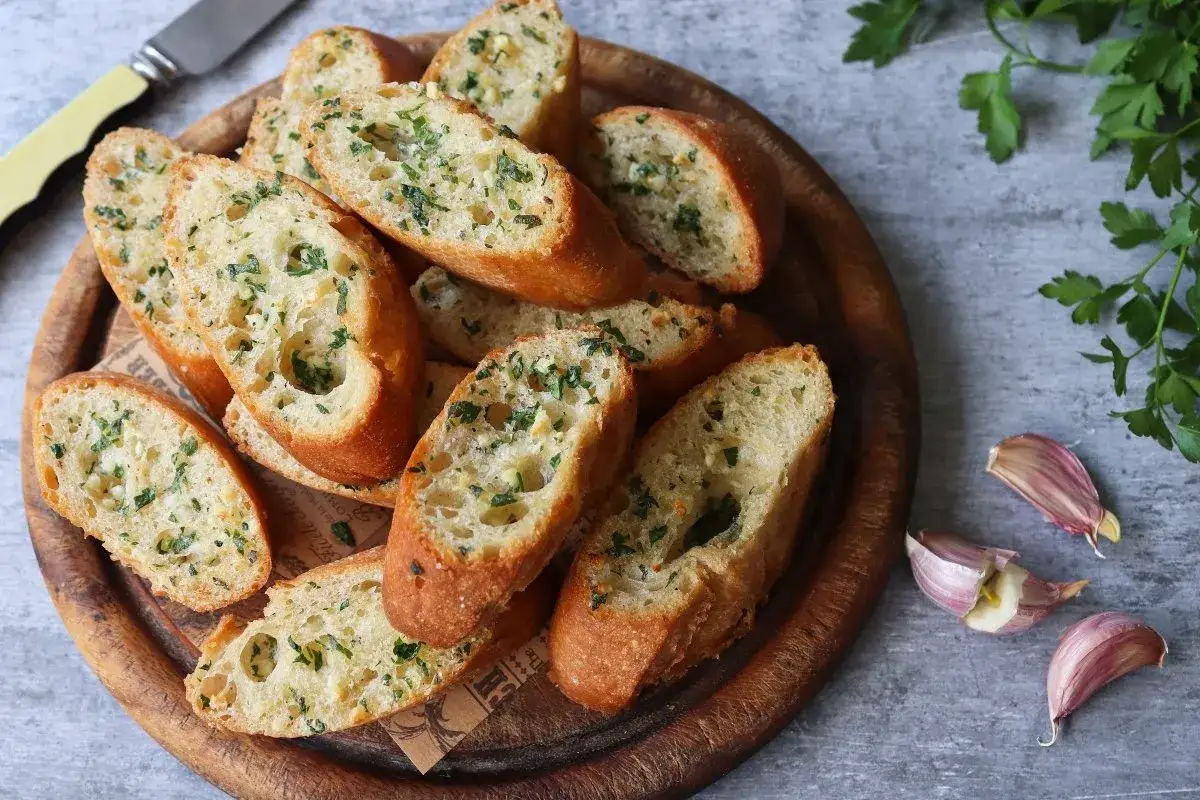Rebanadas de pan de ajo reci&eacute;n horneado, con perejil picado y trozos de ajo visibles.