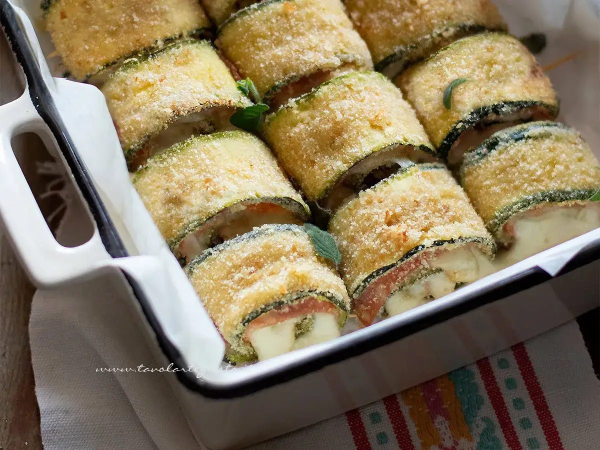 Involtini di zucchine dorati e croccanti, ripieni di formaggio filante e prosciutto, pronti per essere gustati.