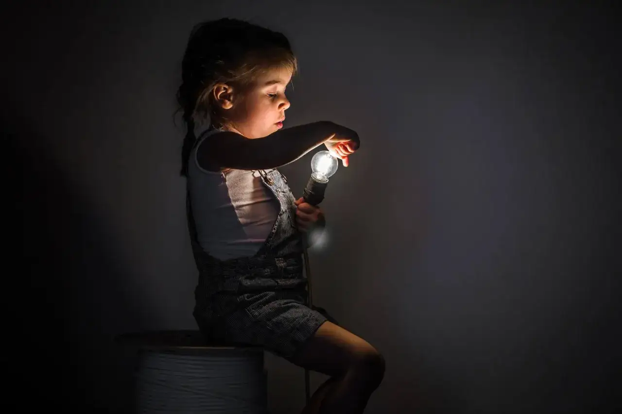 Niña de 2 años, con miedos nocturnos, ilumina la oscuridad con una bombilla.