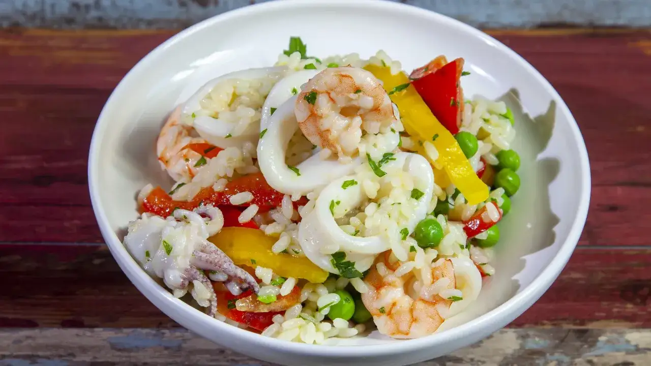 Deliziosa insalata di riso con pesce, gamberi, anelli di calamaro, peperoni e piselli, guarnita con prezzemolo fresco.