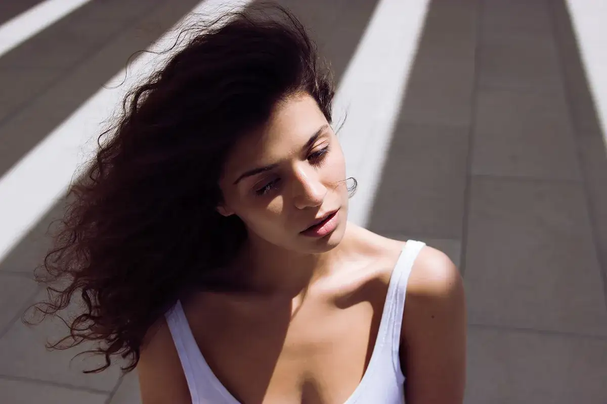 Autoritratto fotografico di una giovane donna con capelli scuri mossi, illuminata da luci oblique.