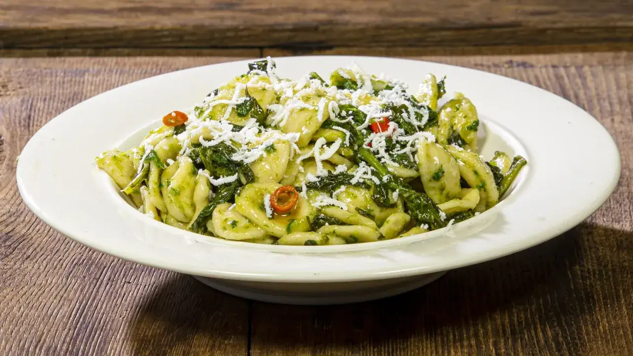 Piatto di orecchiette cime di rapa, condite con un pesto verde e spolverate di formaggio grattugiato.