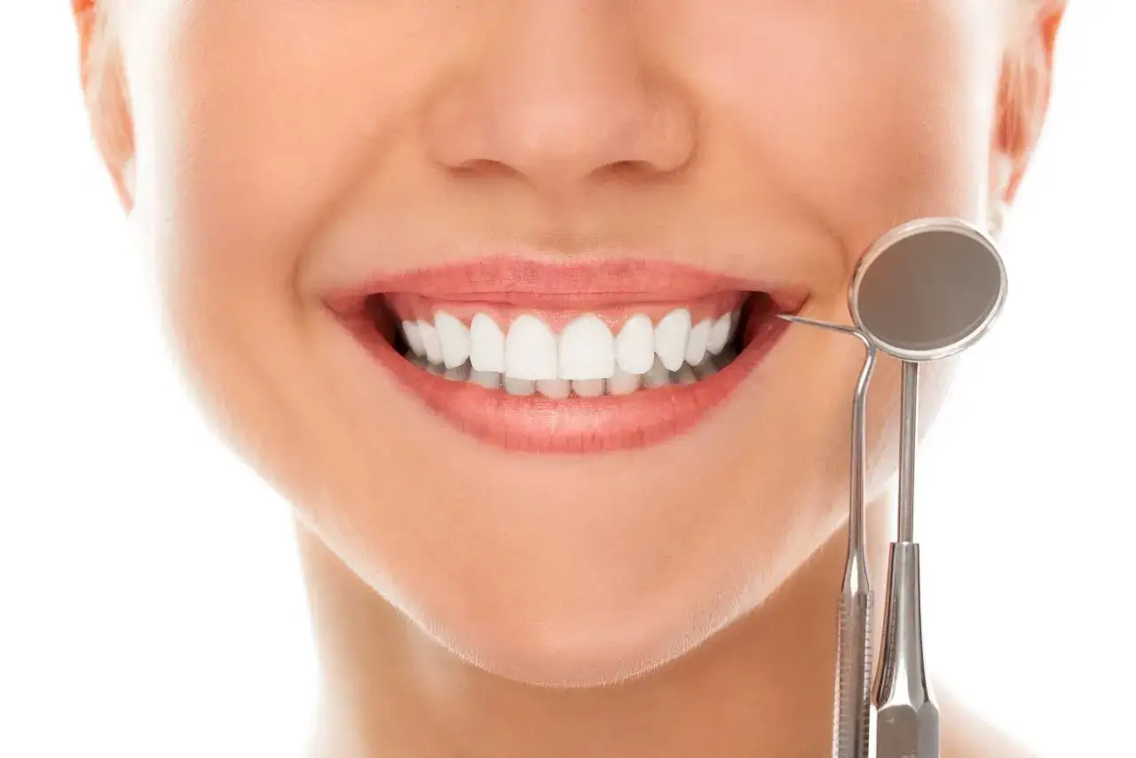 Sonrisa con dientes blancos y alineados, listos para brackets. Un espejo dental examina la dentadura.