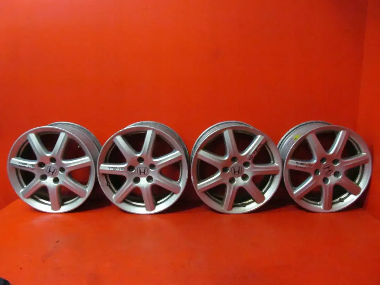Cztery aluminiowe felgi do Honda Civic Si, z logo Hondy i 7 ramionami, prezentują się świetnie na czerwonym tle.