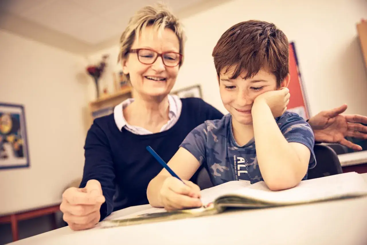 Ein freundlicher Integrationshelfer unterst&uuml;tzt einen Jungen beim Lernen. Das Gehalt f&uuml;r diese wichtige Arbeit ist oft nicht hoch, aber die Freude am Erfolg der Kinder ist unbezahlbar.