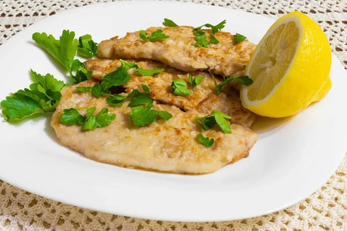 Scaloppine di maiale dorate, guarnite con prezzemolo fresco e spicchio di limone, pronte per essere gustate.