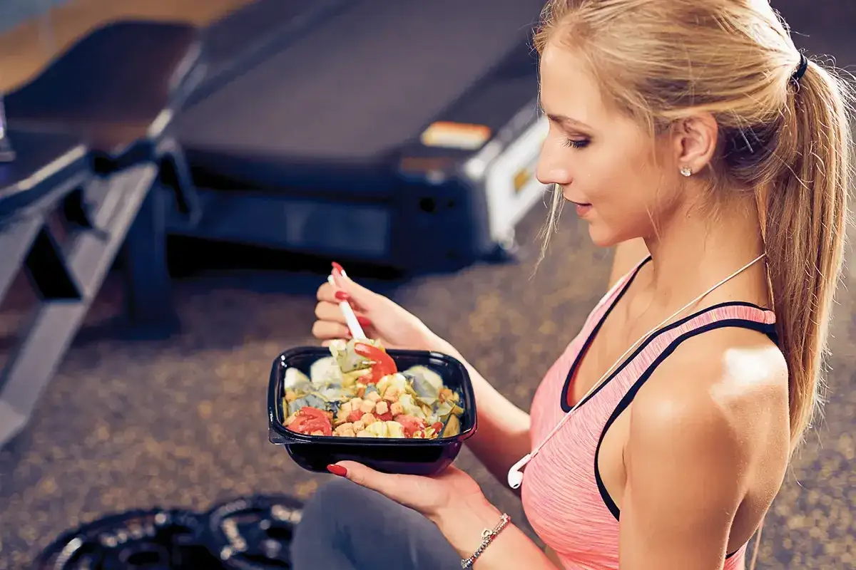 Junge Frau isst gesunden Salat nach dem Training. Sie achtet auf ihre Ernährung, um Fett und Kalorien zu kontrollieren.