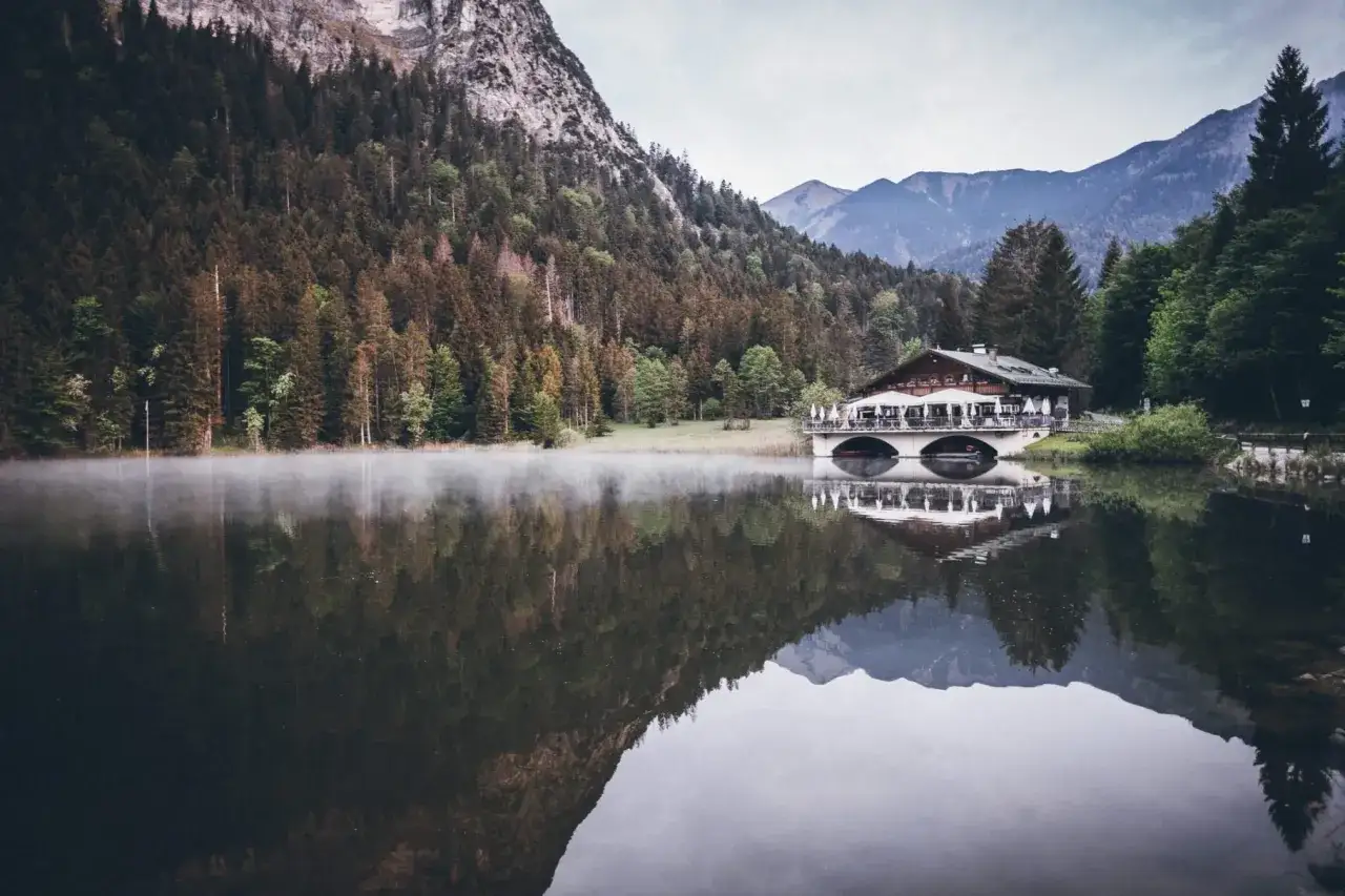 Ein idyllischer See mit Nebelschwaden, ein Gasthaus am Ufer und Berge im Hintergrund – ein echter Geheimtipp Garmisch-Partenkirchen.