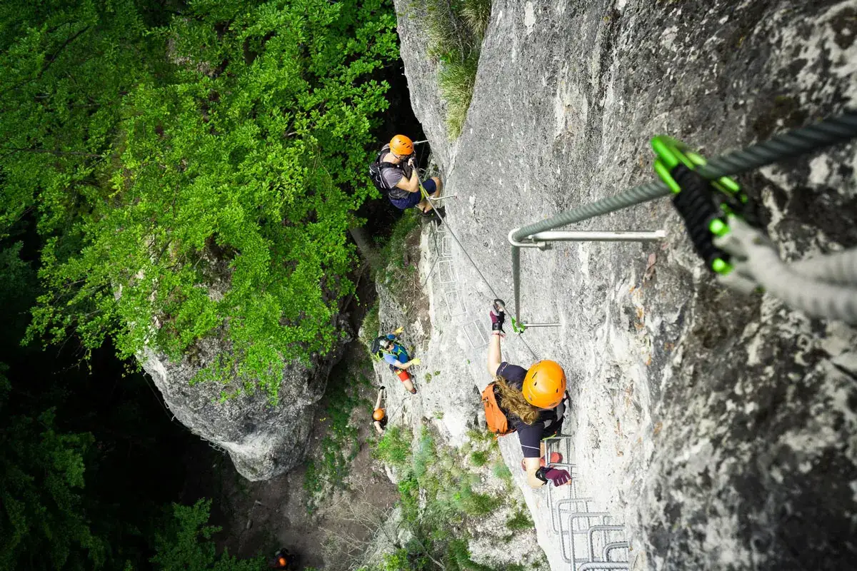 Wspinaczka na via ferrata Słowacja. Grupa osób pokonuje skalną ścianę, używając stalowych lin i drabinek.