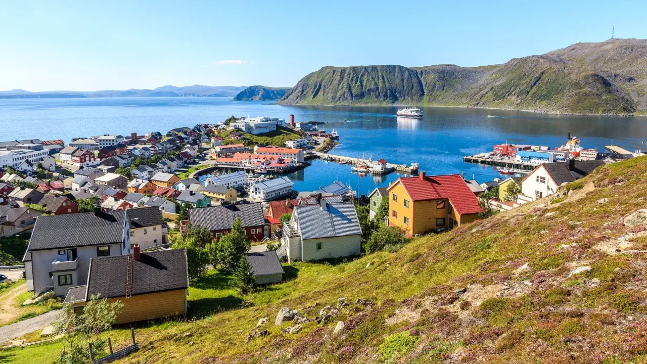 F&auml;rgglada hus i en kuststad vid en fjord, med ett stort fartyg i bakgrunden. Detta &auml;r Norges nordligaste stad, Honningsv&aring;g.