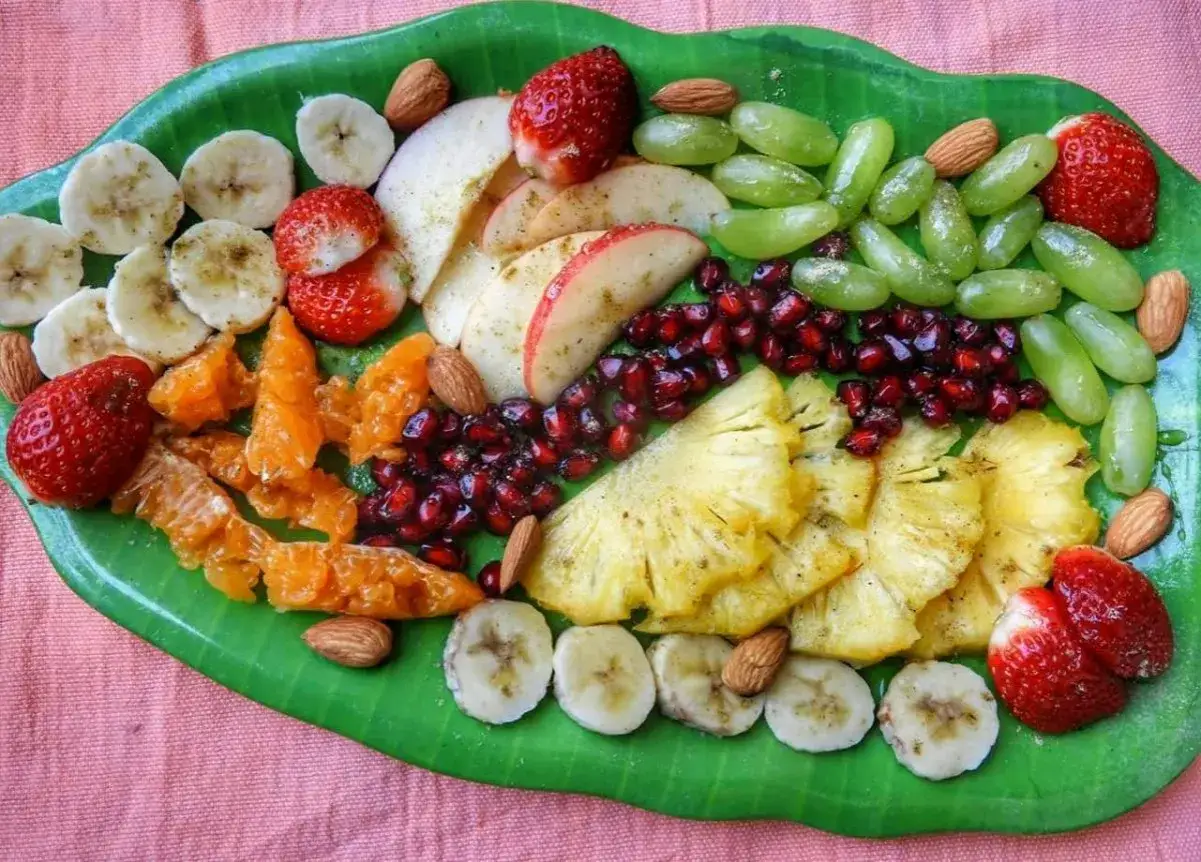 Eine bunte obstplatte einfach arrangiert mit Erdbeeren, Trauben, Ananas, Bananen, Granatapfelkernen, Mandeln und Mandarinenstücken.