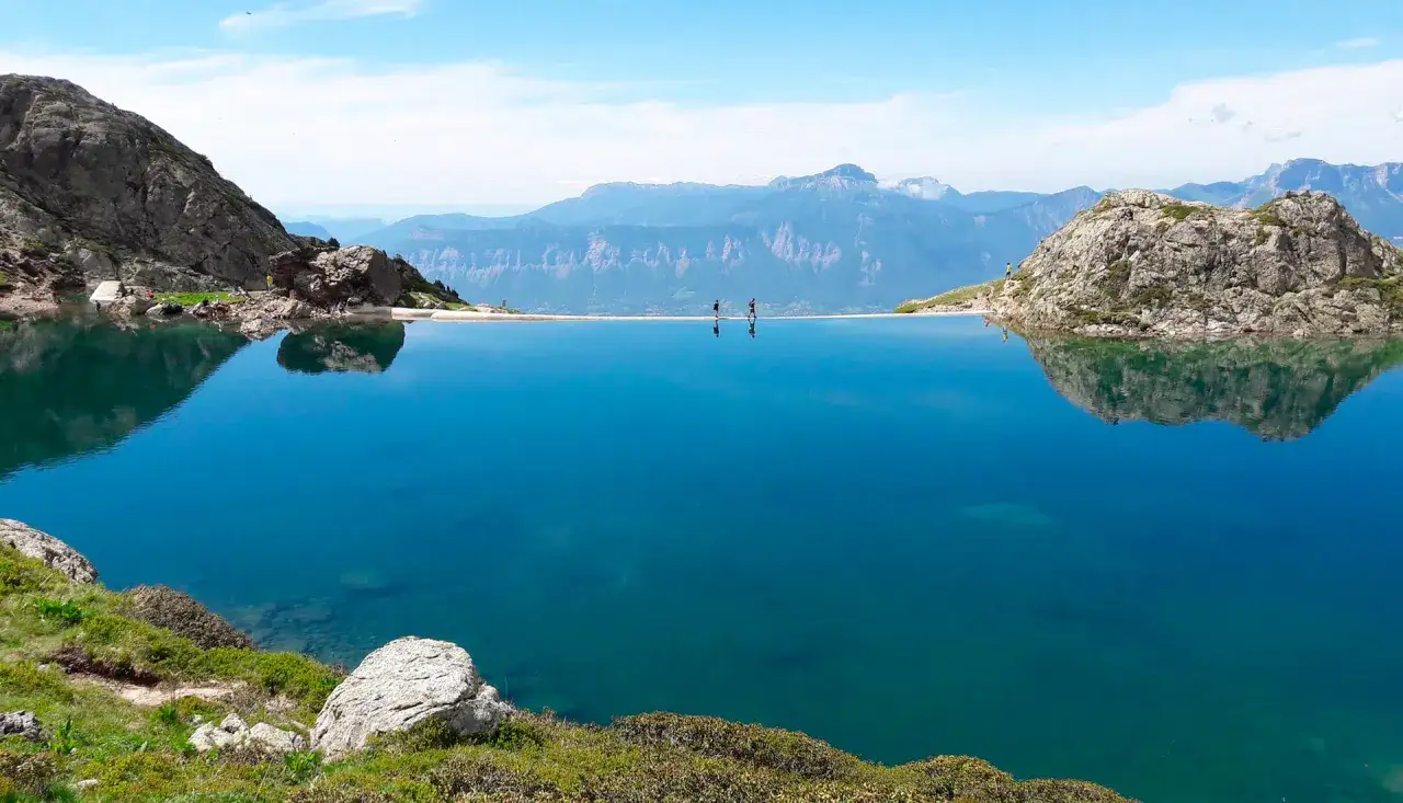 Lac alpin aux eaux bleues intenses, reflets des montagnes. Des randonneurs profitent du paysage, un moment **gr 738** de sérénité.