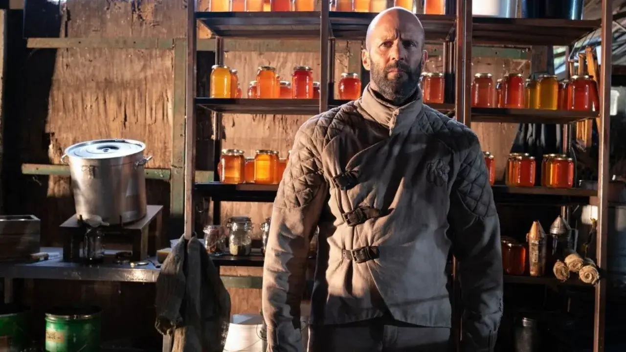 Jason Statham jako pszczelarz w filmie. W tle półki pełne słoików z miodem i sprzęt pszczelarski.
