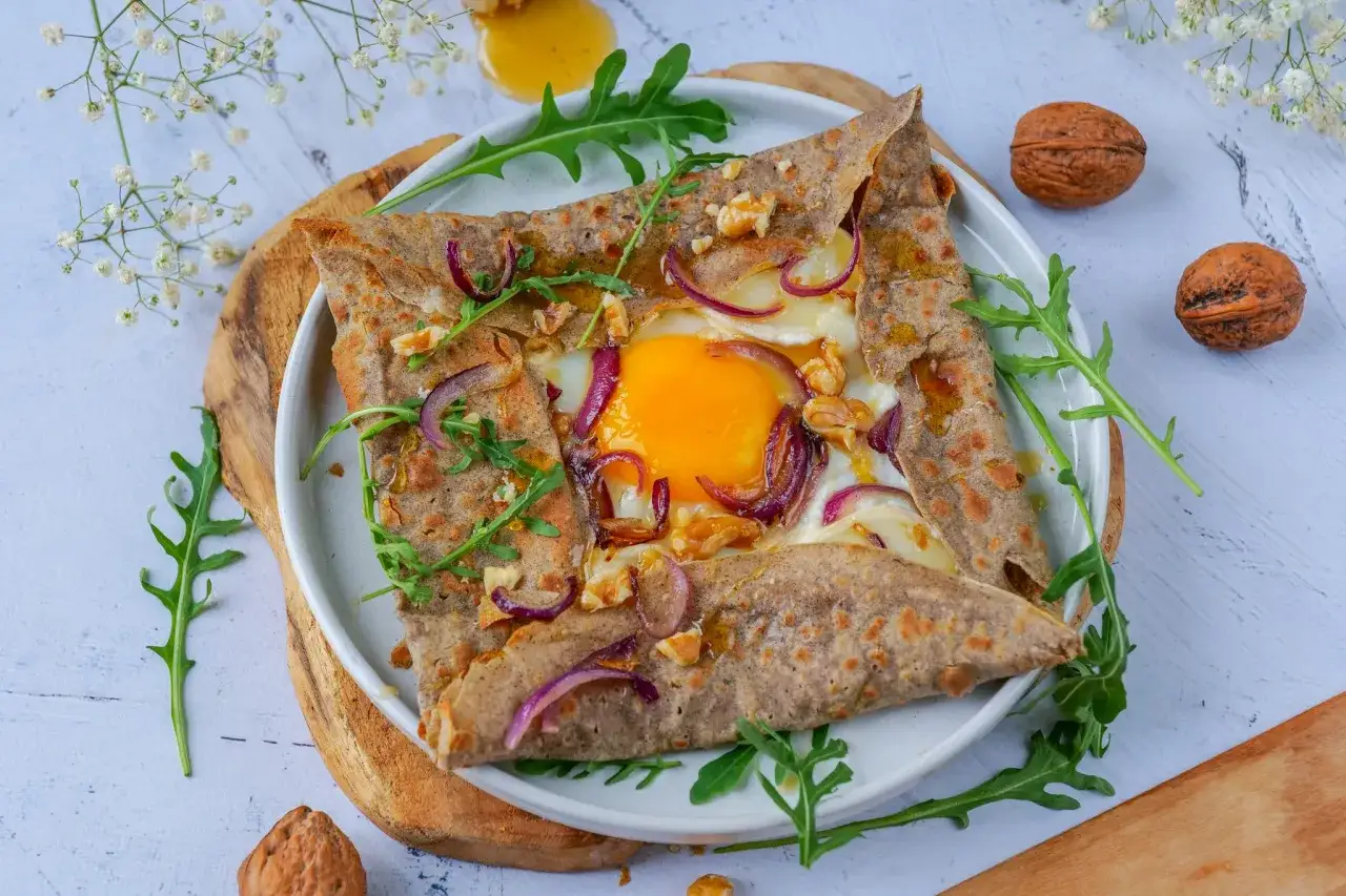 Délicieuse galette sarrasin garnie d'un œuf coulant, oignons rouges, noix et roquette. Un délice pour les papilles !