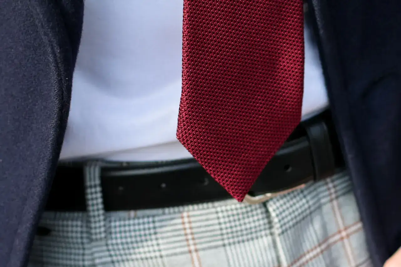 Ciemnogranatowa marynarka, biała koszula i bordowy, dzianinowy krawat tworzą stylowy zestaw. Modne krawaty męskie dodają elegancji.