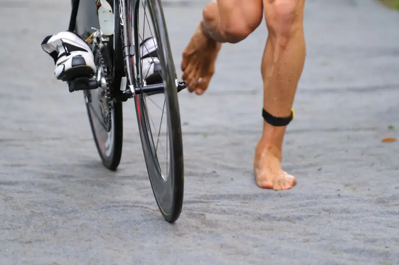 Ein Athlet auf einem Rennrad, barfu&szlig; daneben. Die Frage, wie lange dauert ein Triathlon, besch&auml;ftigt viele.
