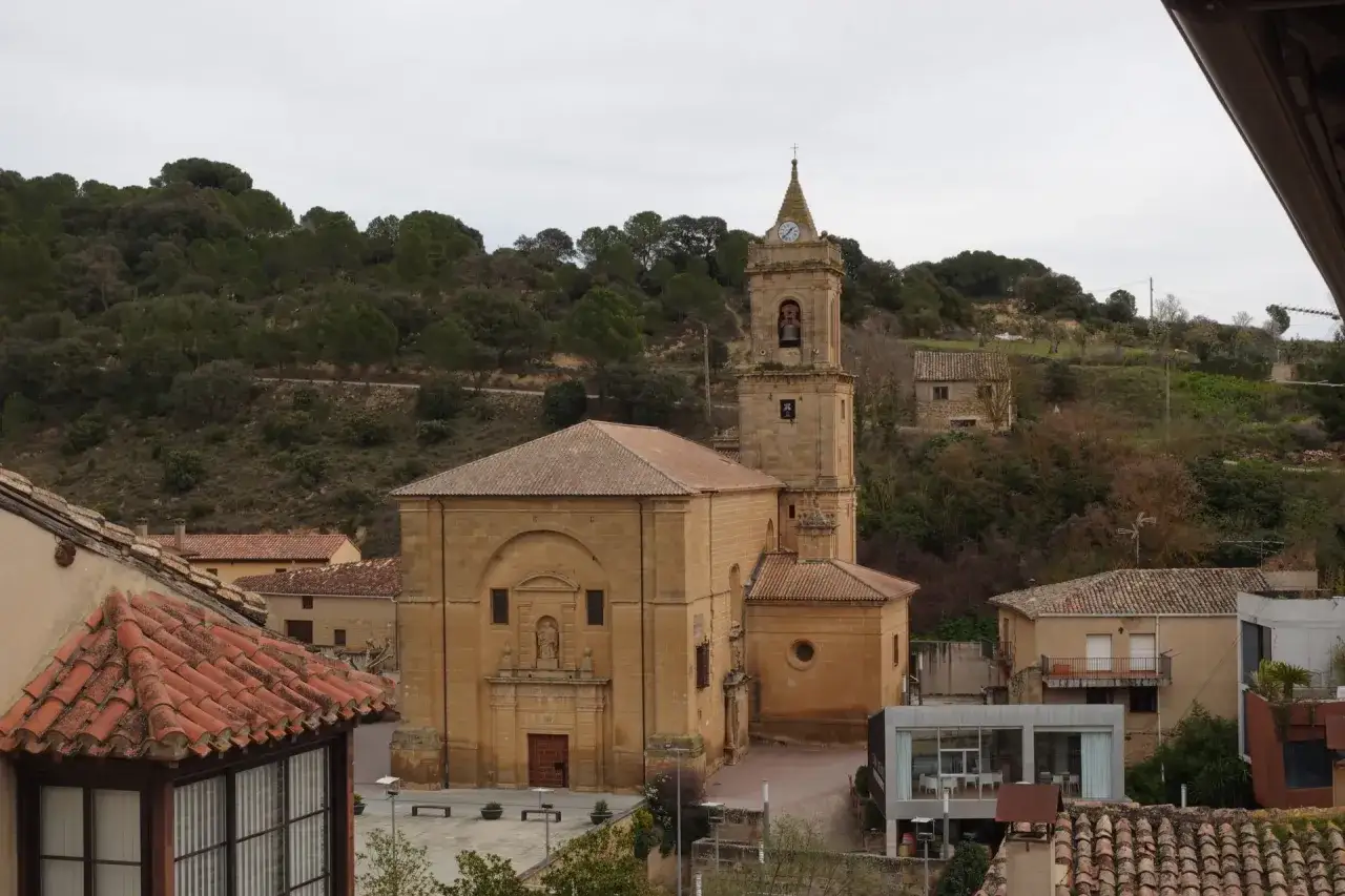 Kirche mit Glockenturm und Uhr in Rioja Alavesa, umgeben von Häusern und bewaldeten Hügeln.