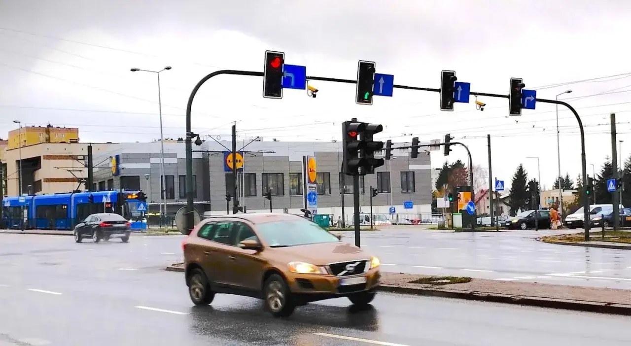 Skrzyżowanie z tramwajem i samochodami. Białe kamery nad światłami monitorują ruch.