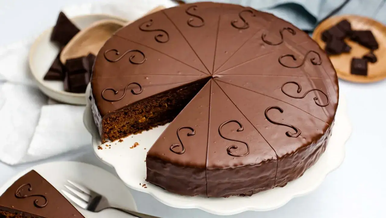 Ein Anschnitt der Sachertorte, die mit Schokolade &uuml;berzogen und mit S-f&ouml;rmigen Verzierungen dekoriert ist. Das sachertorte rezept original ist hier perfekt umgesetzt.