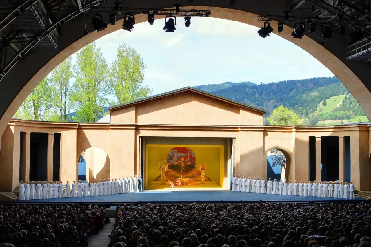 Chor in weißen Gewändern steht auf Bühne, während ein Gemälde mit biblischer Szene im Hintergrund hängt. Ein Schauspiel der Leidenschaften, das die Zuschauer fesselt.