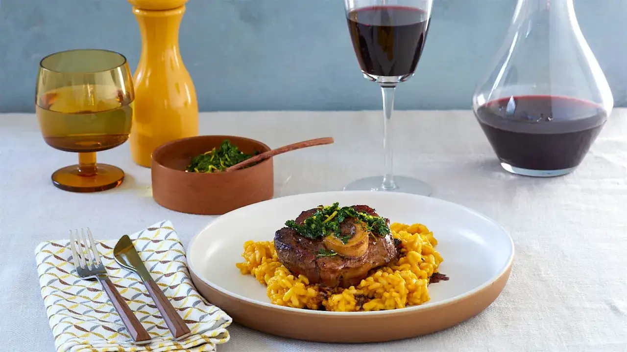 Ein Teller Ossobuco mit Safranrisotto, garniert mit Kr&auml;utern. Dazu passt ein Glas Rotwein.