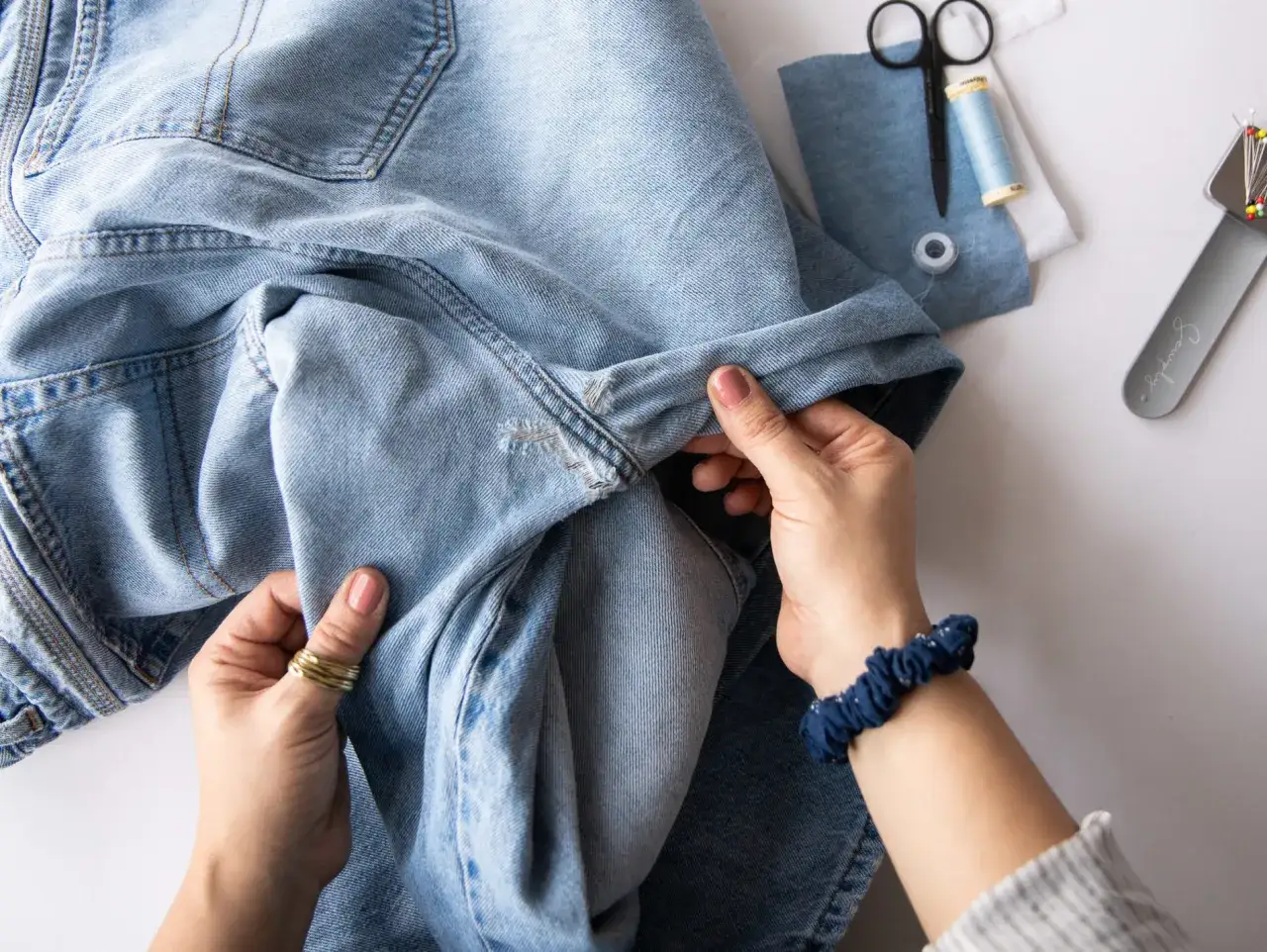 H&auml;nde reparieren ein Loch in Jeans mit einem Flicken. N&auml;hutensilien liegen bereit.