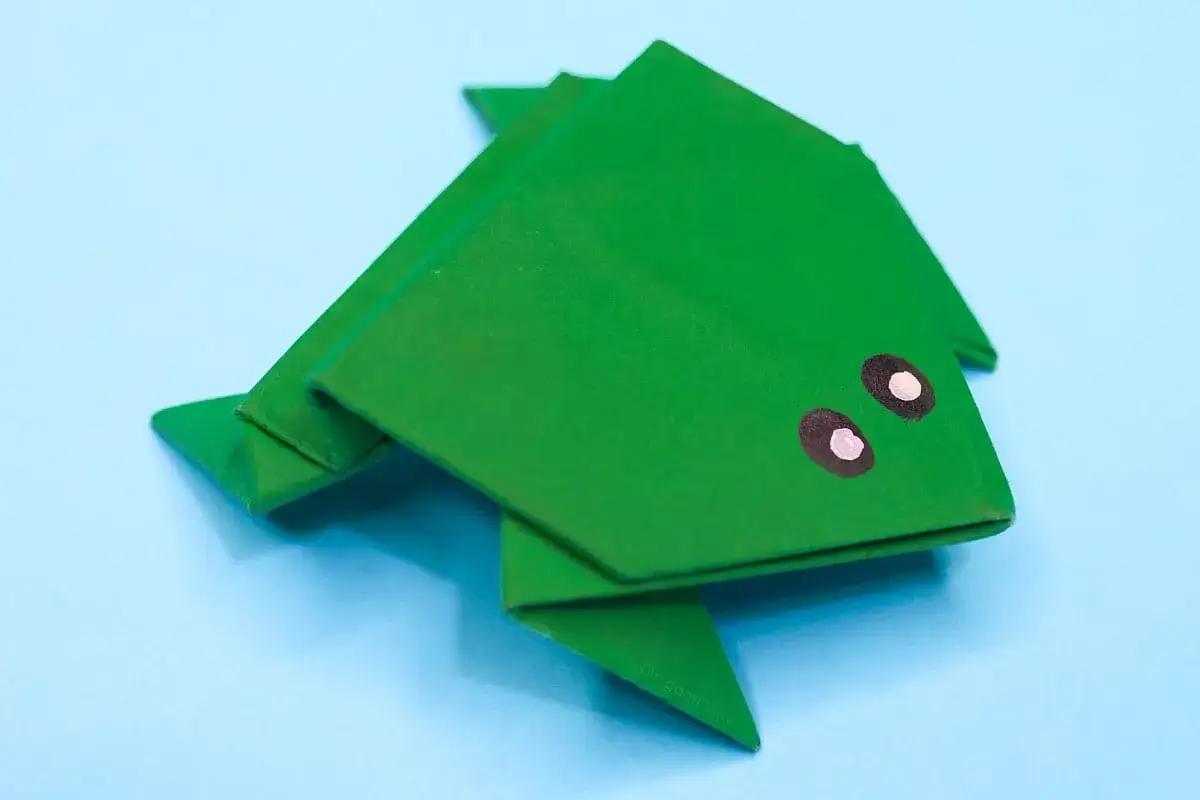 Gr&uuml;ner Origami-Frosch mit aufgemalten Augen. Eine einfache Frosch falten Kindergarten anleitung f&uuml;r kleine Bastler.