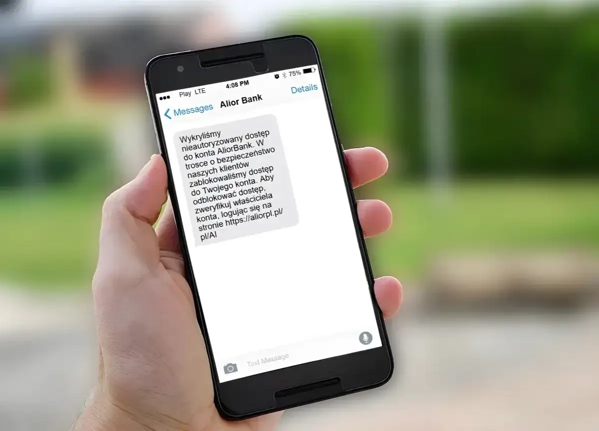 Dłoń trzyma smartfon z wiadomością od Alior Bank o rzekomym nieautoryzowanym dostępie. To przykład spoofingu, próby wyłudzenia danych.