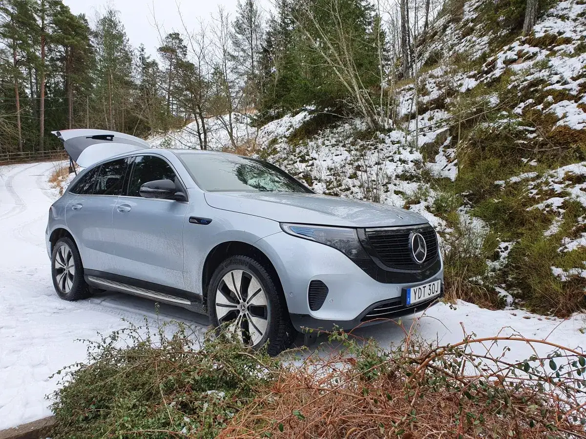 En silverfärgad EQC Mercedes står parkerad på en snöig skogsväg i Sverige. Bagageluckan är öppen.