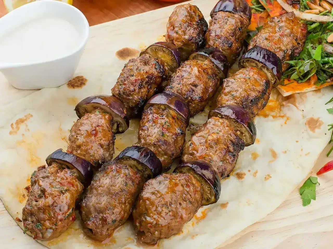 Kofta kebab z bakłażanem na patyku, podany z sosem i pitą. Pyszne danie, które zachwyci każdego miłośnika kuchni bliskowschodniej.