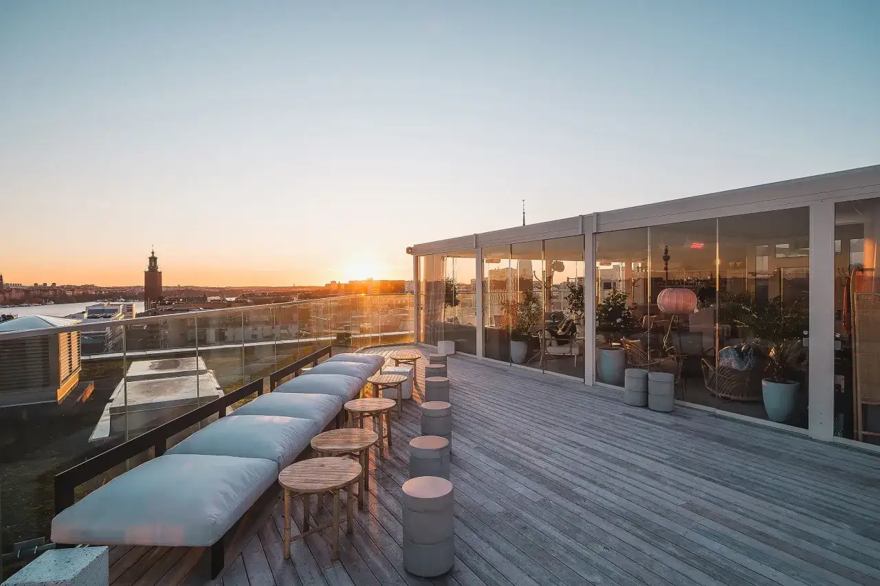 En takterrass i Stockholm med solnedgång över stadens silhuett. En arc blique by nobis-inspirerad design med bekväma sittplatser och glaspartier.